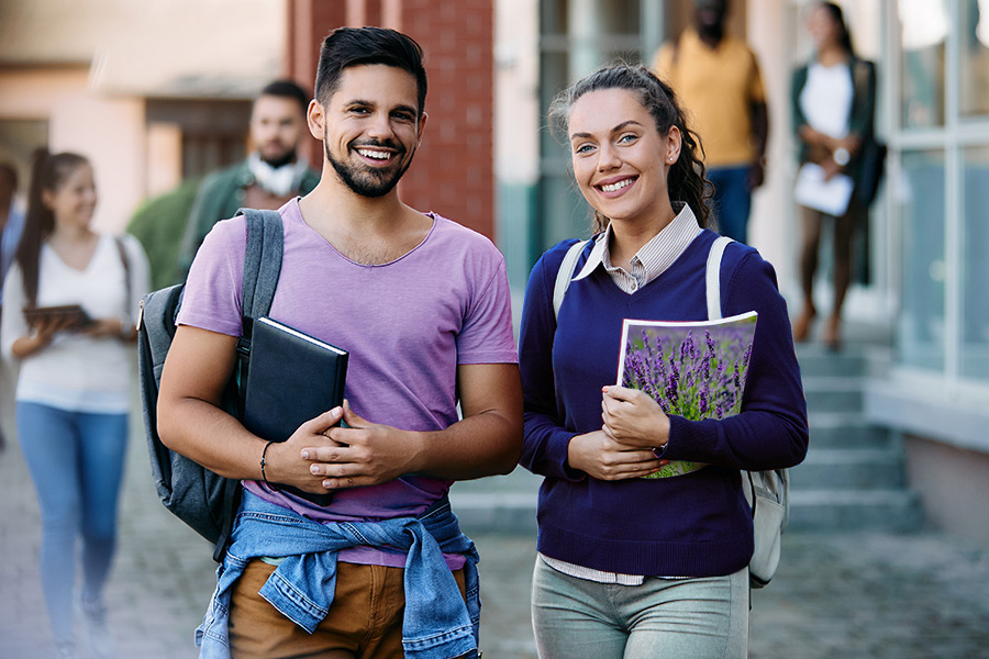 2 college students smiling. One student is wearing a lavender color t-shirt and the other student is holding a notebook that has a field of lavender pictured on the back of it.